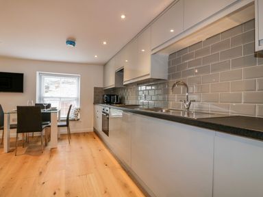 A kitchen with white cabinets black countertop gray tile backsplash and a dining table with chairs at The Crows Nest in Mevagissey