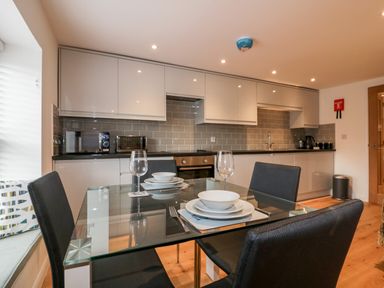 A kitchen with white cabinets a glass dining table with place settings and black chairs at The Crows Nest in Mevagissey