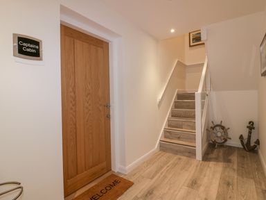 A hallway with a wooden door labeled Captains Cabin and stairs with nautical decorations at Captains Cabin in Mevagissey