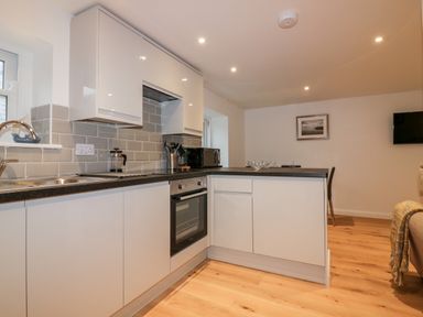 A kitchen with white cabinets gray backsplash and wooden floor at Captain's Cabin in Mevagissey