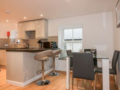 A kitchen with a counter and two bar stools next to a dining table with four chairs and a window at Captains Cabin in Mevagissey