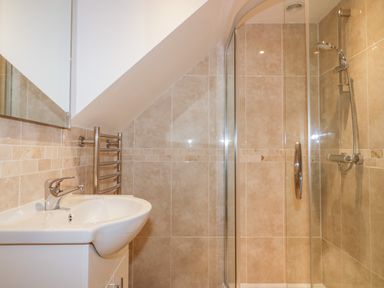 A bathroom with a sink, mirror, heated towel rail and a glass-enclosed shower at Captains Cabin in Mevagissey