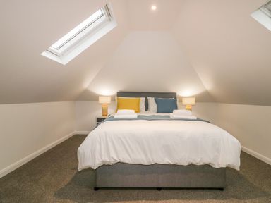 A bedroom with a bed two bedside tables two lamps and skylight windows at Captain's Cabin in Mevagissey