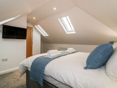 A bedroom with a bed folded towels two skylight windows a wall-mounted television and a wooden door at Captains Cabin in Mevagissey