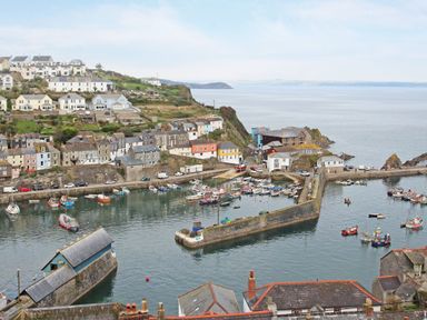 A coastal scene with boats in a harbor and houses on the hillside at Captain's Cabin in Mevagissey