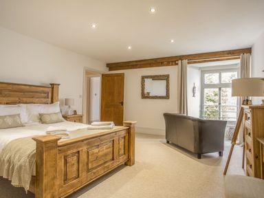 A bedroom with a wooden bed and bedside tables a leather chair and a window at The Penthouse Lynmouth Bay in Lynton