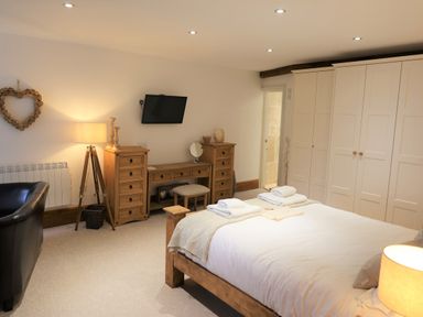 A bedroom with a wooden bed, white wardrobes, a wooden desk with drawers, a black armchair, a lamp, and a wall-mounted TV at The Penthouse Lynmouth Bay in Lynton