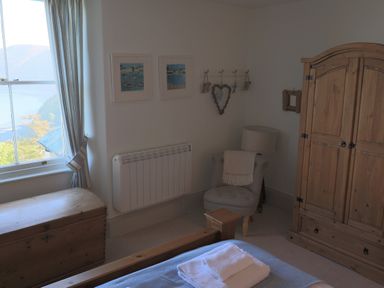 A bedroom corner with a wooden wardrobe a chair with a blanket a wooden chest and a window with curtains at The Penthouse Lynmouth Bay in Lynton