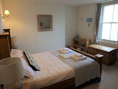 A bedroom with a wooden bed with folded towels on it a wooden chest and bookshelf near a window at The Penthouse Lynmouth Bay in Lynton