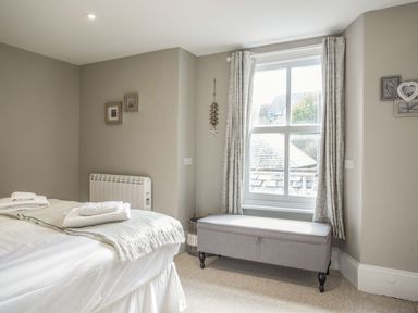 A bedroom with a bed folded towels a window with curtains and a bench at The Penthouse Lynmouth Bay in Lynton
