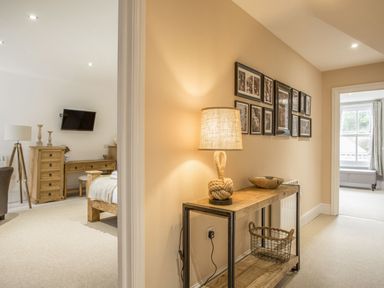 A hallway with a wooden console table and lamp next to a doorway leading to bedrooms at The Penthouse Lynmouth Bay in Lynton