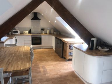 A kitchen with wooden countertops white cabinets a dining table and chairs under a sloped ceiling at The Penthouse Lynmouth Bay in Lynton