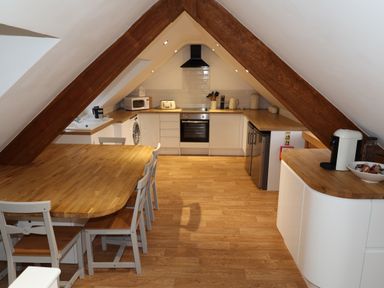 A kitchen with wooden table and chairs under slanted ceiling with wooden beams at The Penthouse Lynmouth Bay in Lynton
