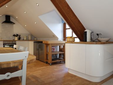 A kitchen with wooden floor wooden dining table white chairs and white cupboards at The Penthouse Lynmouth Bay in Lynton