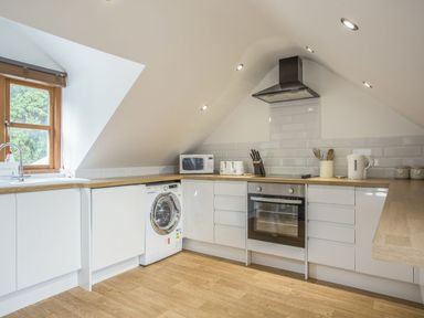 A kitchen with white cabinets a washing machine an oven microwave and wooden countertops at The Penthouse Lynmouth Bay in Lynton