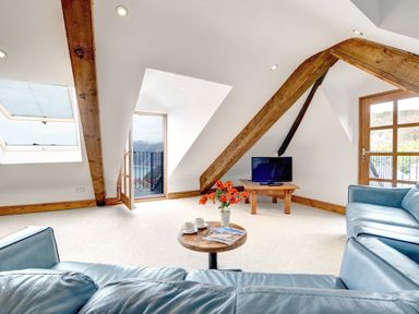 A living room with blue sofas a small wooden table with flowers and cups a television on a wooden stand and exposed wooden beams at The Penthouse Lynmouth Bay in Lynton