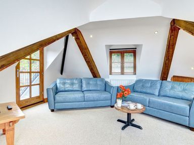 A sitting area with two blue sofas a small round table with cups and flowers and a wooden door and window at The Penthouse Lynmouth Bay in Lynton