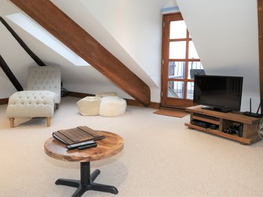 A living room with a wooden coffee table remote controls a TV on a wooden stand a chaise lounge and a door leading outside at The Penthouse Lynmouth Bay in Lynton