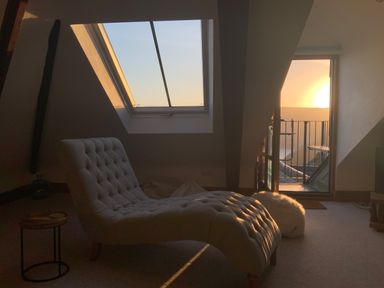 A room with a chaise lounge chair under a skylight window and an open door leading to a balcony at The Penthouse Lynmouth Bay in Lynton