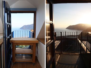 A kitchen area with a wooden island and an open door leading to a balcony with a metal railing overlooking the sea and hills a balcony with a small round table and benches overlooking the sea and hills at The Penthouse Lynmouth Bay in Lynton