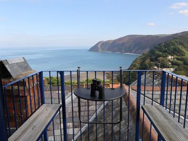 A balcony with blue railing and benches overlooking the sea and hills at The Penthouse Lynmouth Bay in Lynton