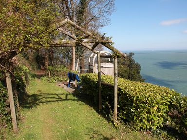 A garden path with wooden arch trellis and a blue bench overlooking the sea at The Penthouse Lynmouth Bay in Lynton