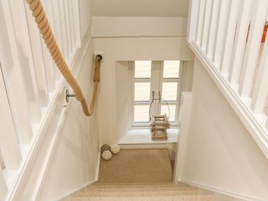 A staircase with beige carpet and rope handrail leading to a window with decorative balls and a lantern at The Penthouse Lynmouth Bay in Lynton