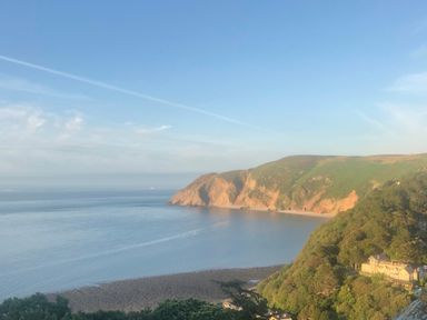 A coastal view with cliffs trees and a building near the shore at The Penthouse Lynmouth Bay in Lynton