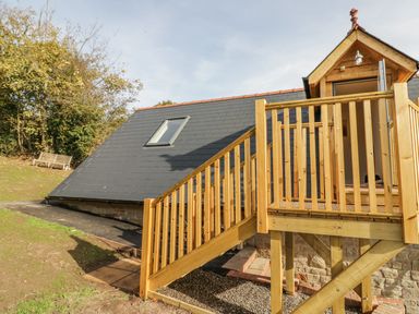 A wooden staircase leading to an elevated porch with a door on a building with a slate roof and a skylight at The Lookout in Llangrove