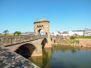 A stone bridge over a river with people walking and a historic stone gatehouse at The Lookout in Llangrove
