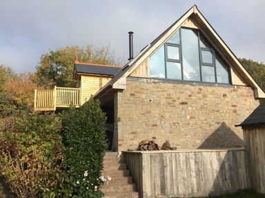 A stone and wood house with large triangular windows and a wooden deck surrounded by greenery at The Lookout in Llangrove