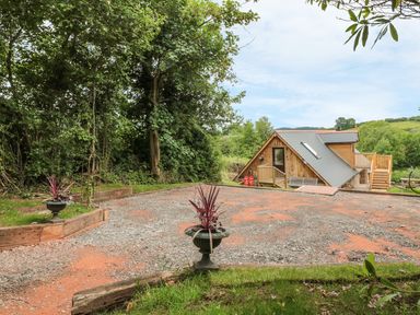 A gravel driveway with planters and a wooden house with a sloped roof in a rural setting at The Lookout in Llangrove