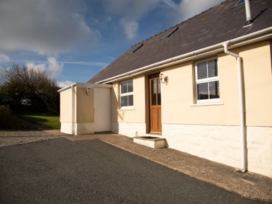 The exterior of a beige house with a wooden door two windows and a small attached structure at Bramble Cottage in Newgale