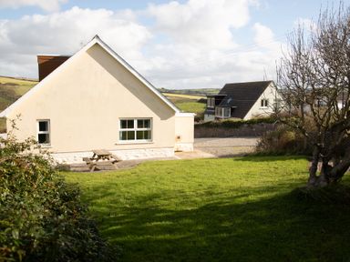 A garden area with grass and a wooden picnic table beside a cream colored house at Bramble Cottage in Newgale