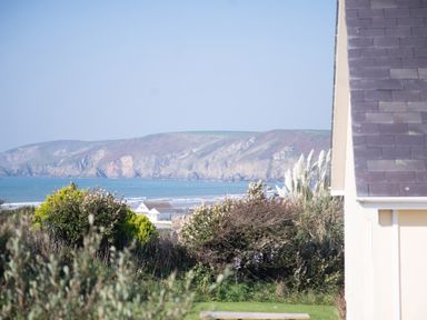 A coastal landscape with bushes a house roof and cliffs in the background at Bramble Cottage in Newgale