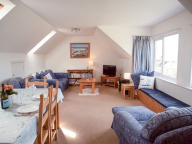 A living room with blue sofas a wooden coffee table a dining table with chairs and a window seat at Bramble Cottage in Newgale