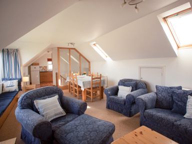 A living room with blue armchairs dining table with chairs and kitchen in the background at Bramble Cottage in Newgale