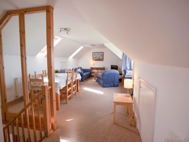 A living area with wooden dining table and chairs and blue upholstered sofas and armchairs at Bramble Cottage in Newgale