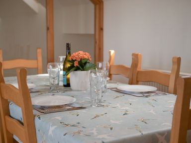 A dining table set with plates glasses a wine bottle and a flower pot at Bramble Cottage in Newgale