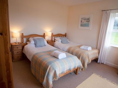 A bedroom with two single beds with checkered blankets and bedside tables with lamps at Bramble Cottage in Newgale