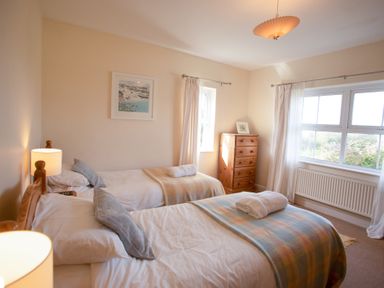 A bedroom with two single beds a wooden chest of drawers and windows with curtains at Bramble Cottage in Newgale