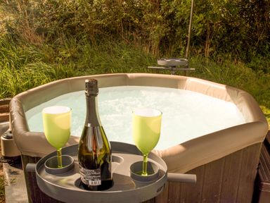 A hot tub with a bottle of sparkling wine and two green glasses at Bramble Cottage in Newgale