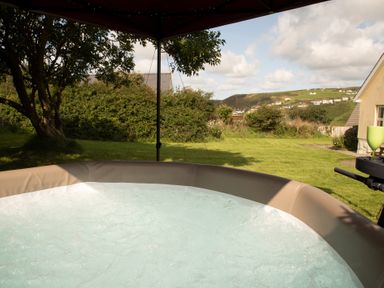 A bubbling hot tub in a garden with grass trees and hills in the background at Bramble Cottage in Newgale