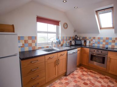 A kitchen with wooden cabinets a refrigerator dishwasher oven and window at Bramble Cottage in Newgale
