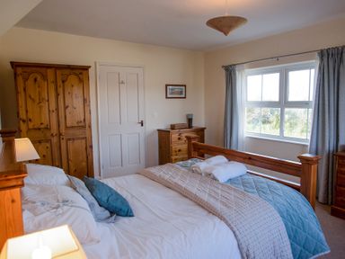 A bedroom with wooden furniture a bed with pillows blankets and rolled towels a window with curtains and framed picture on wall at Bramble Cottage in Newgale
