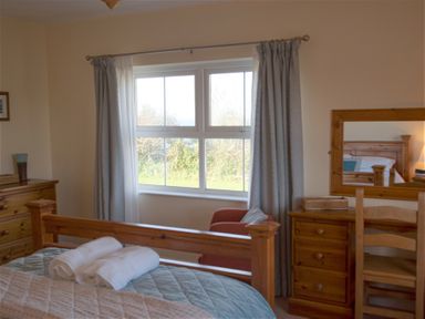 A bedroom with wooden furniture and a window showing greenery outside at Bramble Cottage in Newgale