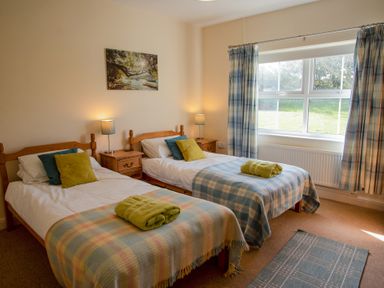 A bedroom with two single beds bedside tables lamps and a window with curtains at Bramble Cottage in Newgale