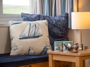 A seating area with pillows and a wooden side table with teapot cups and a lamp at Bramble Cottage in Newgale