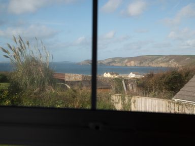 A coastal view with houses cliffs and vegetation seen through a window at Bramble Cottage in Newgale