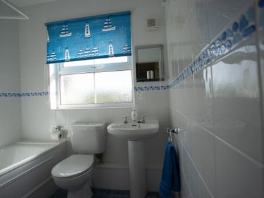 A bathroom with a toilet sink bathtub and blue themed window blind and towel at Bramble Cottage in Newgale